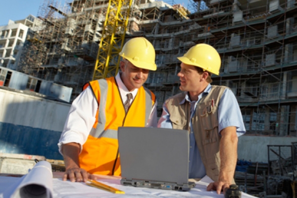 two men in hard hats looking at a laptop.